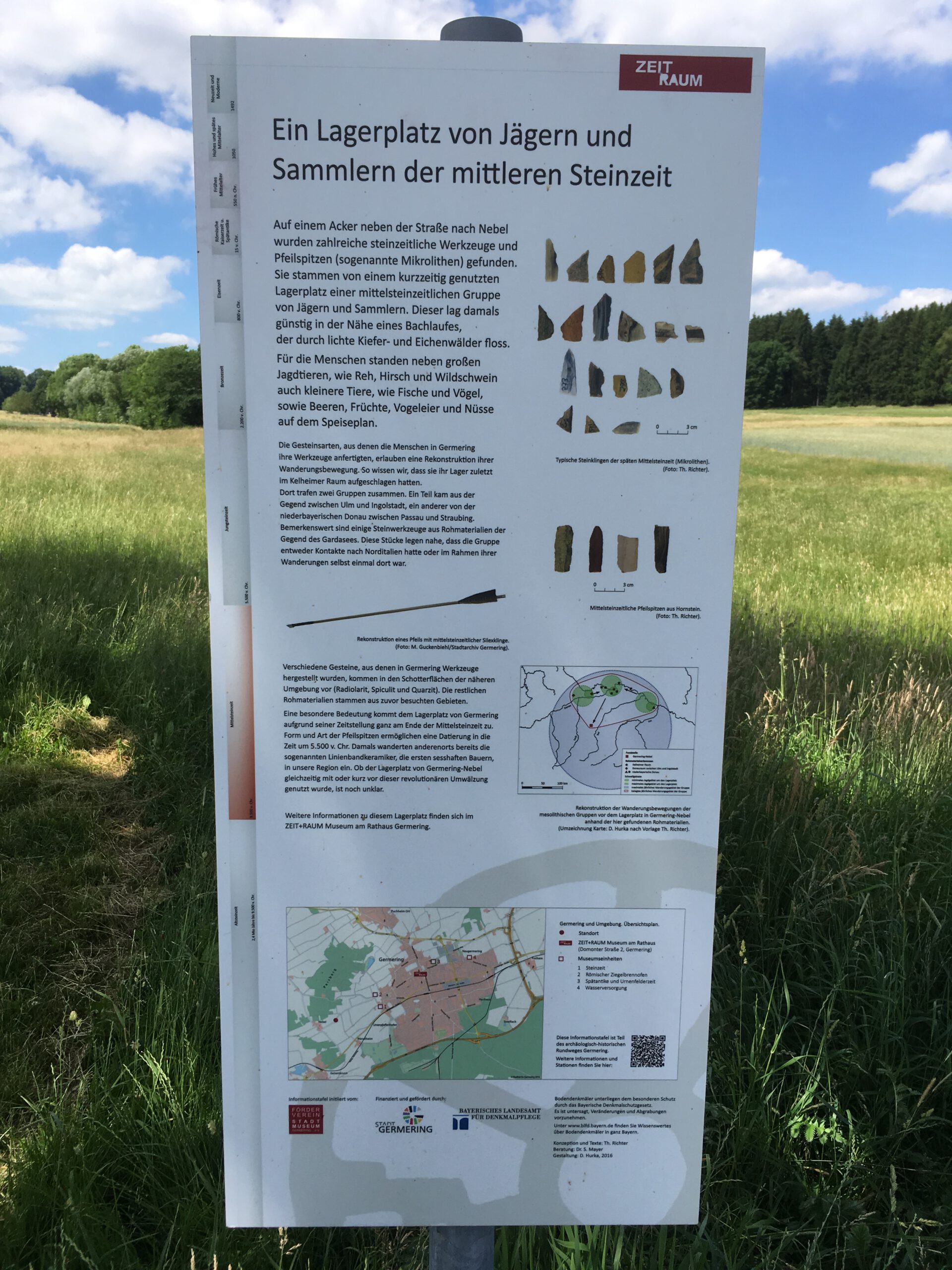 Infotafel am Feldrand bei Germering mit dem Titel „Ein Lagerplatz von Jägern und Sammlern der mittleren Steinzeit“. Sie beschreibt archäologische Funde wie Mikrolithen, die auf einen prähistorischen Lagerplatz hinweisen. Abbildungen zeigen typische steinzeitliche Werkzeuge sowie Karten zur Fundregion. Die Tafel ist Teil der Radrundewege