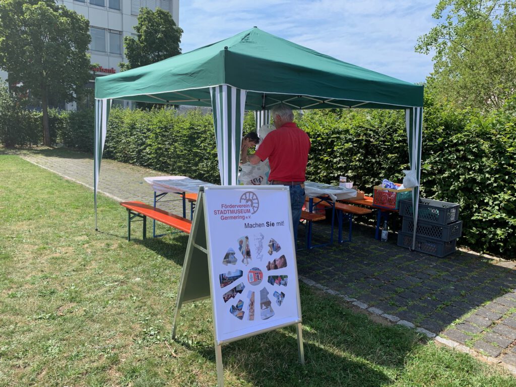 Infostand des F&ouml;rdervereins Stadtmuseum Germering beim Stadtfest. Unter einem gr&uuml;nen Pavillon modellieren Kinder mit Ton kleine Gef&auml;&szlig;e. Im Vordergrund steht ein Aufsteller mit dem Logo des F&ouml;rdervereins und der Aufschrift &bdquo;Machen Sie mit!&ldquo;.