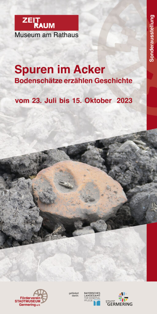 Vorderseite eines Flyers zur Sonderausstellung „Spuren im Acker – Bodenschätze erzählen Geschichte“ im Museum ZEIT+RAUM in Germering vom 23. Juli bis 15. Oktober 2023. Gezeigt wird ein Fundstück aus Tonerde im Boden.